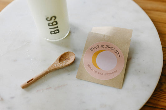 A packet of mothership milk freeze dried breastmilk, a spoon and a bottle on a marble slab.